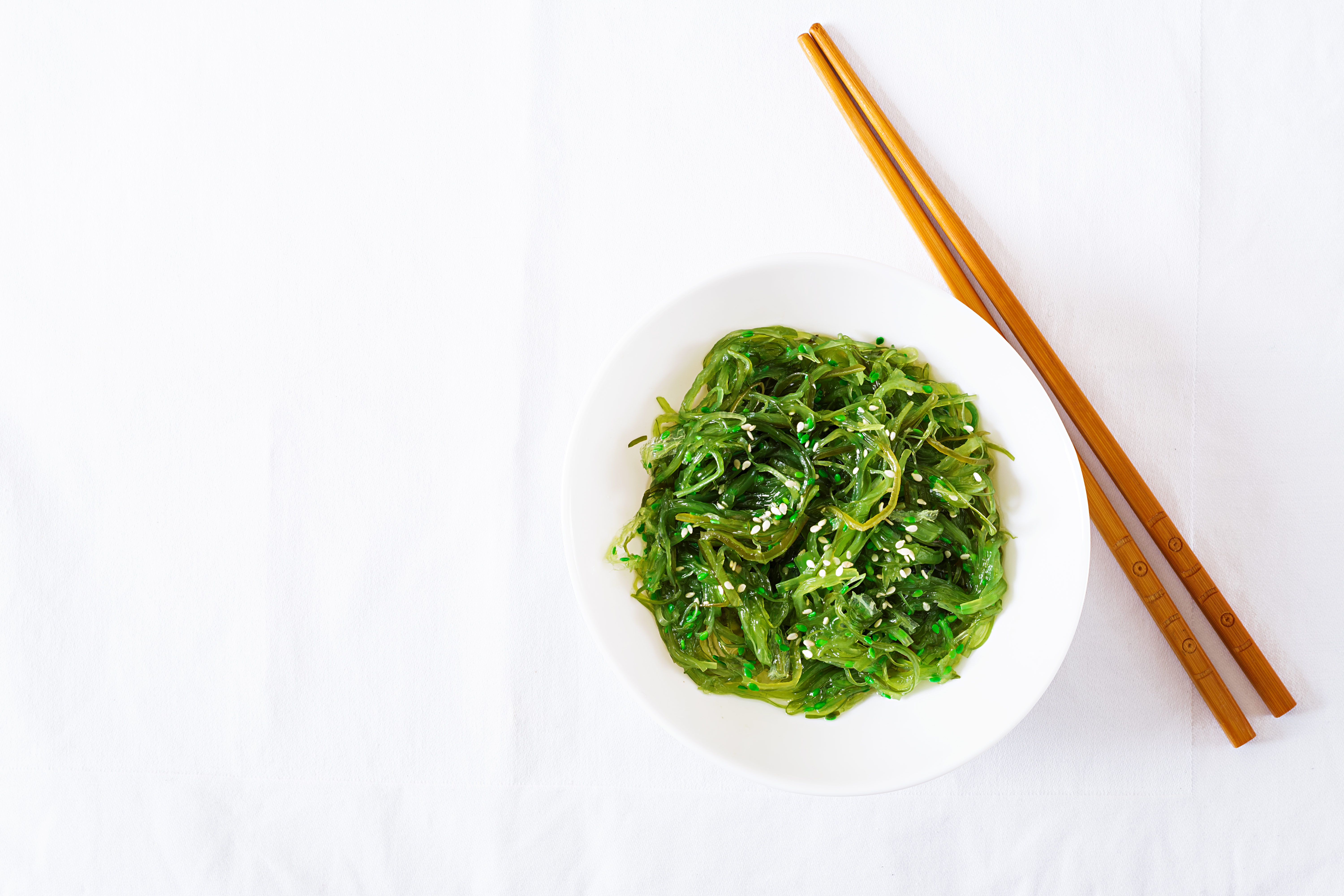 wakame-chuka-seaweed-salad-with-sesame-seeds-bowl-white-table-traditional-japanese-food-top-view-flat-lay