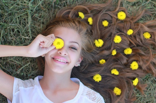 노란색 꽃을 한쪽 눈에 대고 머리카락 위에 노란색 꽃을 올려 놓고 잔디 위에 누워 있는 소녀