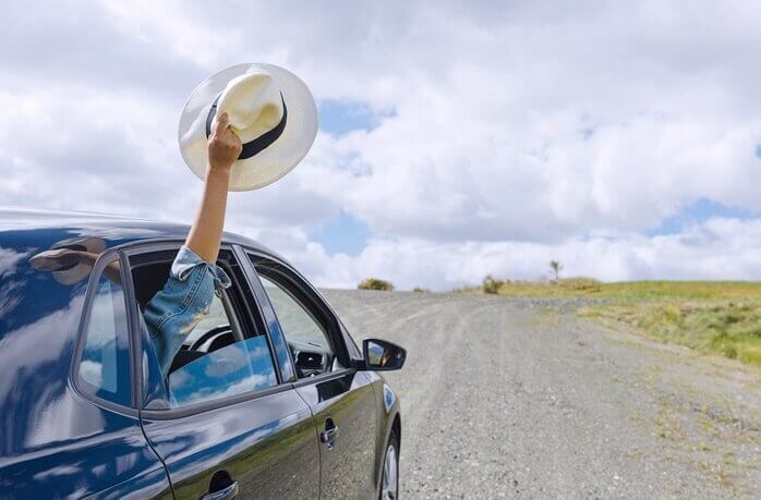 드넓은 벌판을 달리고 있는 차 창문으로 모자를 든 손이 나와 하늘로 뻗고있는 모습