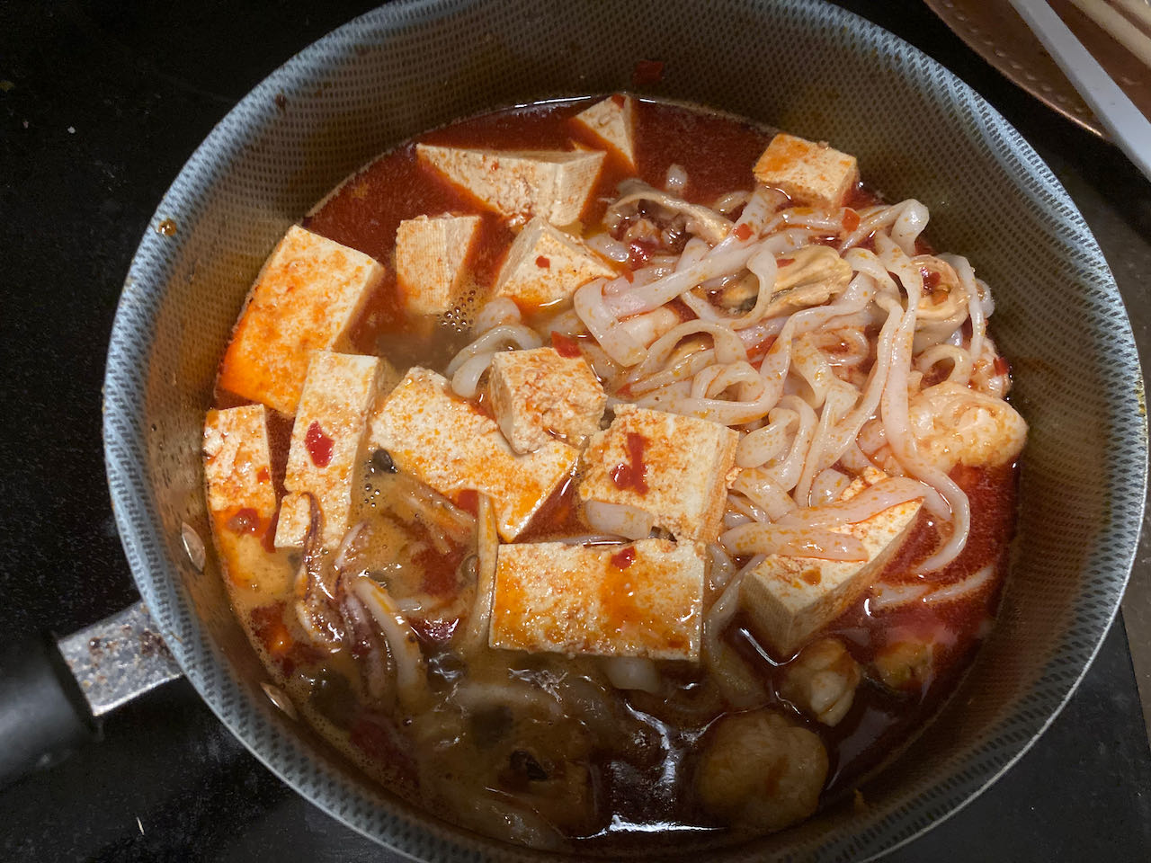 photograph of mala stew, after adding shirataki noodle, tofu and mala sauce.