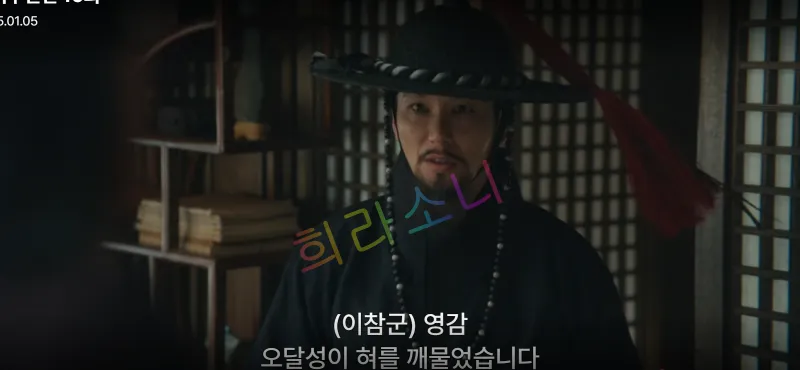 검은 갓을 쓰고 구슬 장식을 두른 남성이 방 안에서 진지한 표정으로 서 있습니다. 주변에는 책과 나무로 된 선반이 보이며&amp;#44; 자막은 &amp;quot;(이참군) 영감&amp;#44; 오달성이 혀를 깨물었습니다.&amp;quot;