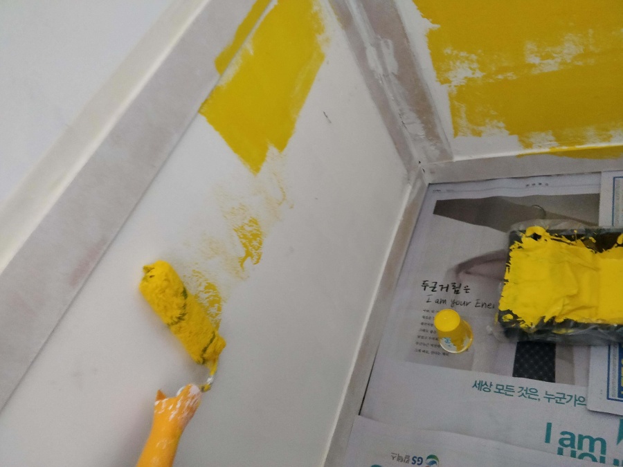 벽에 고정한 격자 웨인스코팅 위로 노란색 페인트를 칠하는 사진