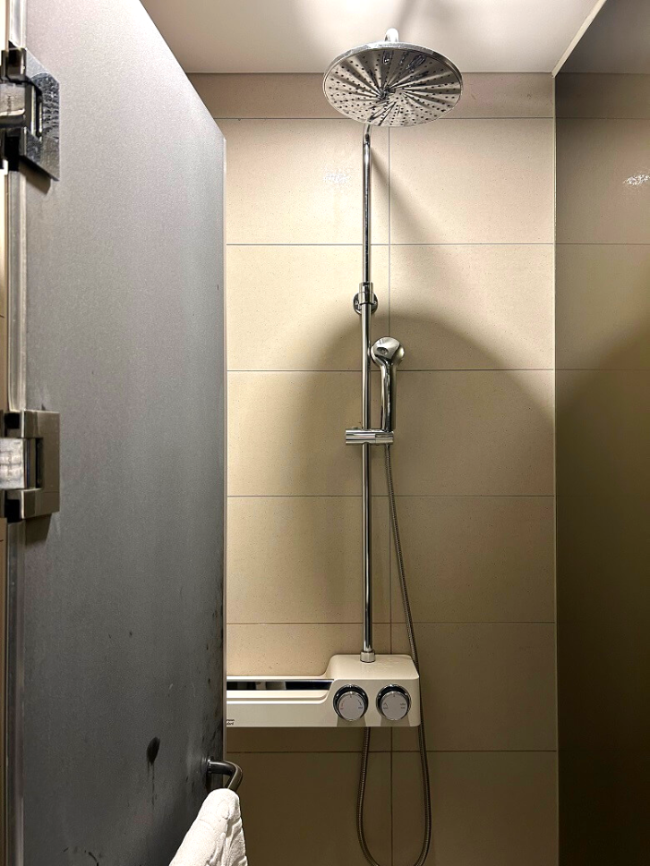 베이지색-타일과-은색-샤워기가-있는-샤워실을-찍은-사진