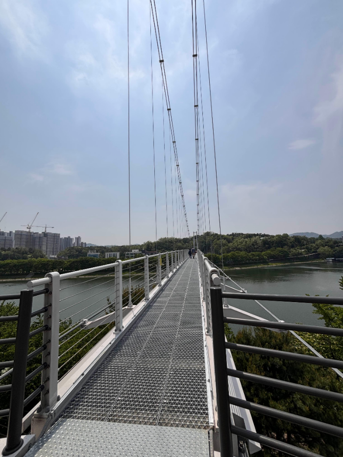춘천 출렁다리 진입 구간, 철제 바닥과 난간, 맑은 하늘 아래 풍경.
Start of the K-Sairo248 bridge in Chuncheon, with metal flooring, railings, and a clear sky backdrop.