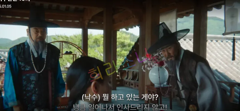 전통적인 누각에서 이낙수와 박준기가 서서 심각한 대화를 나누고 있습니다. 한 남성은 검은 갓을 쓰고 파란색 옷을 입었으며&amp;#44; 다른 한 남성은 회색 옷을 입고 있습니다. 자막은 &amp;quot;(낙수) 뭘 하고 있는 게야? 냉큼 일어나서 인사드리지 않고!&amp;quot; 
