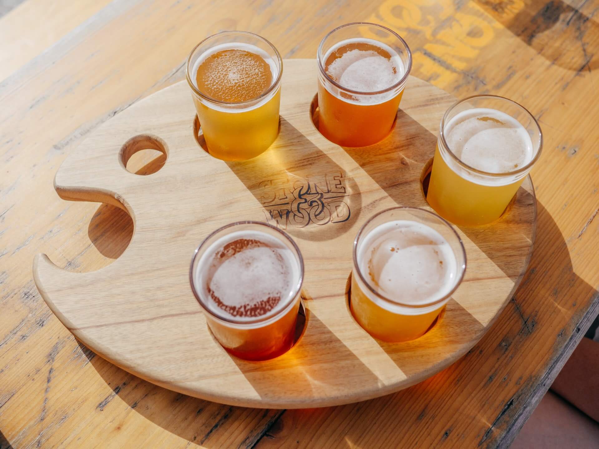나무로된 판에 5개의 맥주가 투명한 컵에 담겨져 있는 사진
