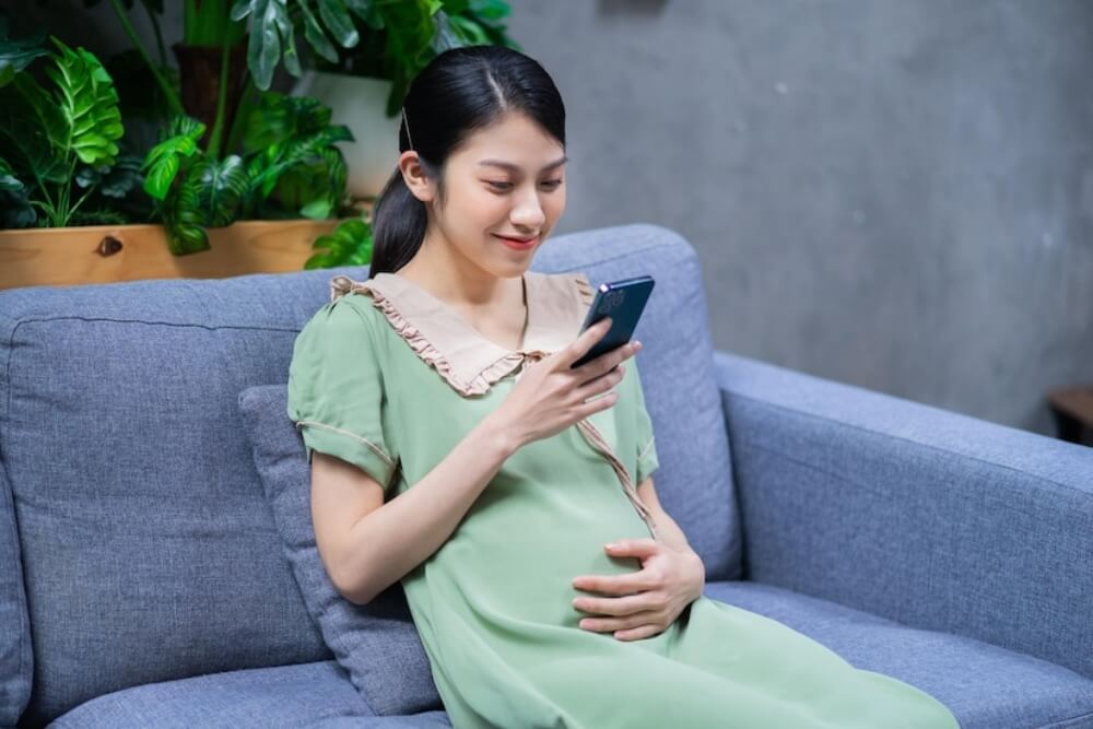 임산부가 쇼파에 앉아서 휴대푠을 보고 있는 이미지