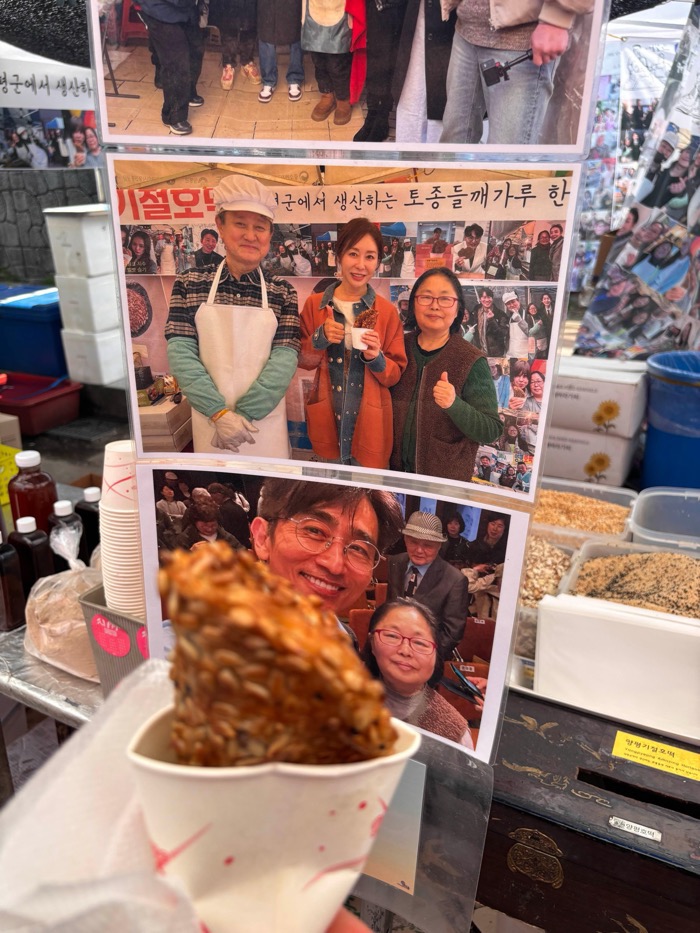 호떡 판매 부스와 판매자 사진 부스 풍경. View of K-Hoddeok vendor booth displaying a photo collage of the sellers and a sesame snack held in front.