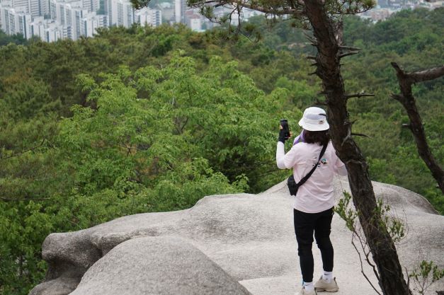 바위에 서 있는 흰옷 상의 검은 바지 입은 여 1&#44; 핸드폰 보고 있음&#44;