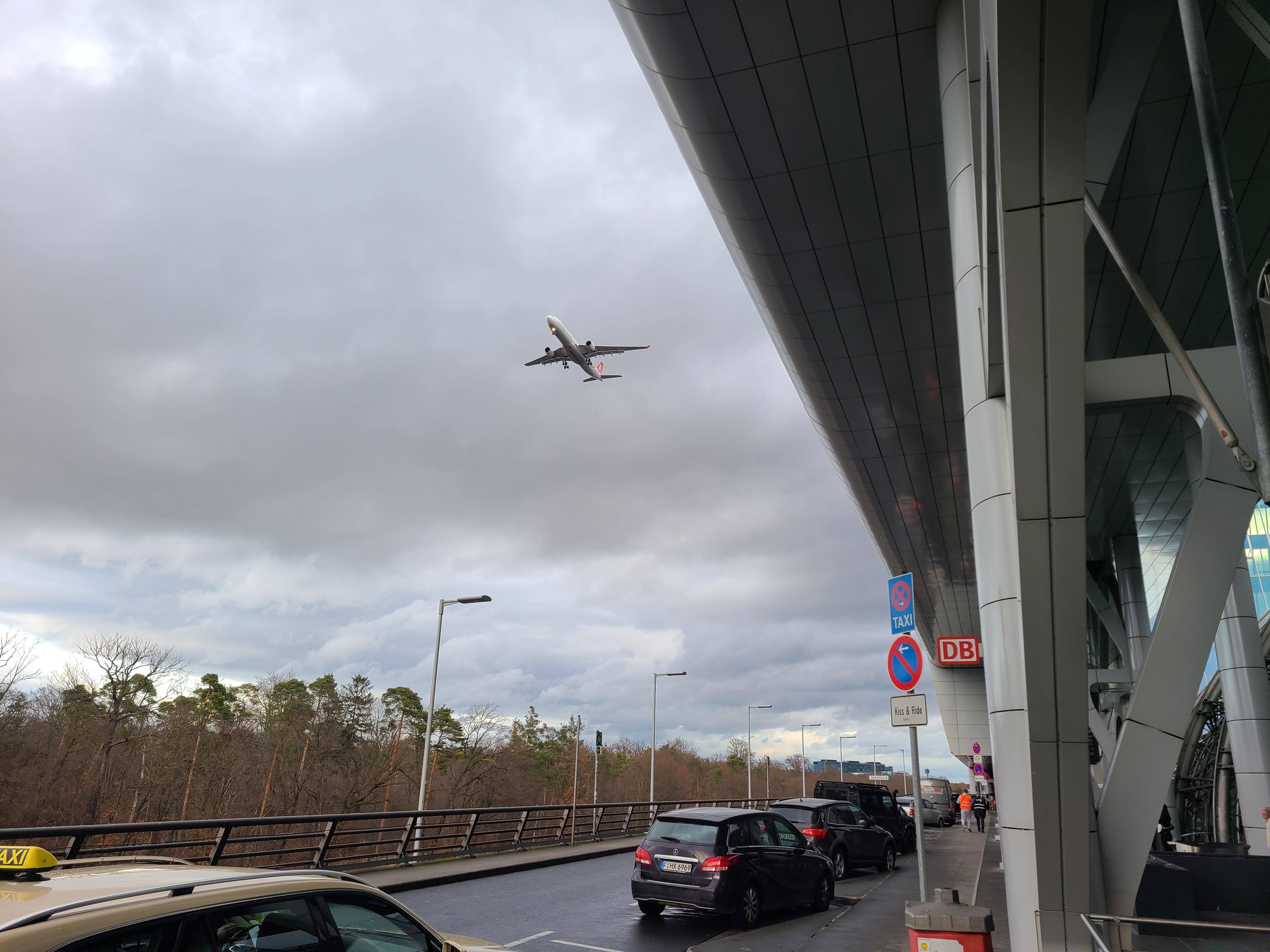 공항 건물밖 주차된 차들과 하늘을 날고 있는 비행기