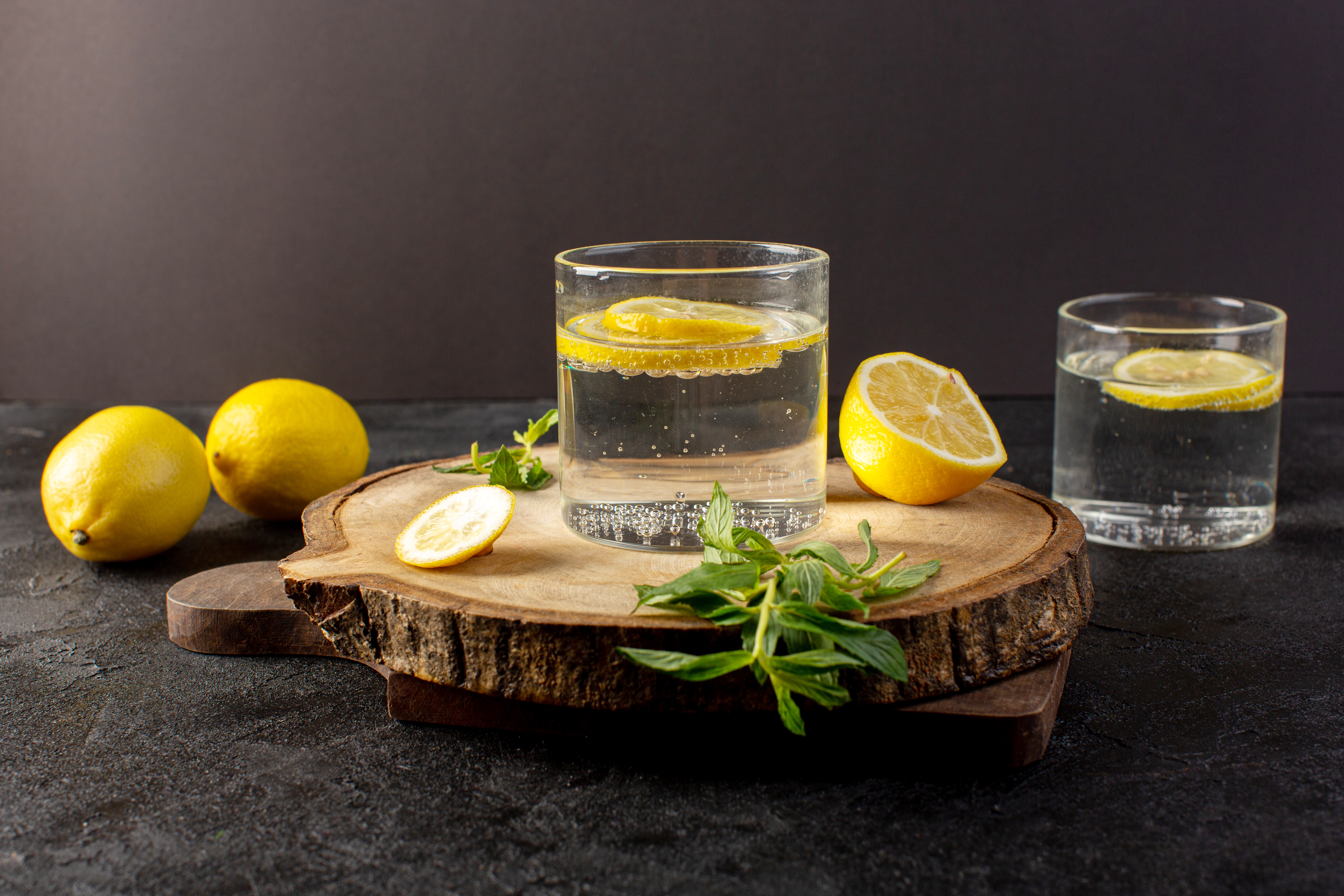 front-view-water-with-lemon-fresh-cool-drink-with-sliced-lemons-along-with-whole-lemons-leaves-inside-transparent-glasses-dark