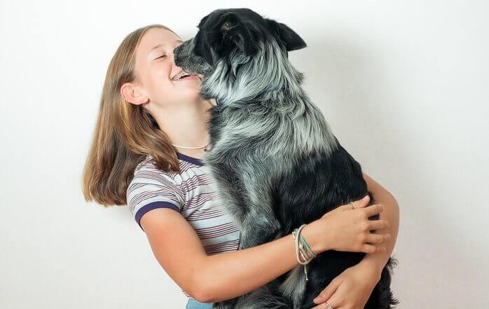 검은색과 회색의 긴 털을 가진 개를 여자 아이가 품에 안고 웃고 있는 모습 