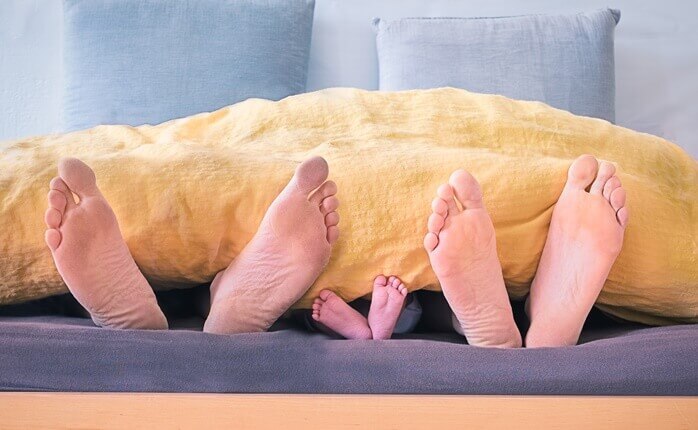 침대 아래쪽에서 바라본 시선으로 남자와 여자의 발바닥&#44; 그리고 가운데에 아기의 발바닥이 보인다.