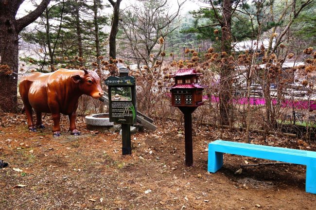 황소 조형물&#44; 연자방아 안내문&#44; 가운데에 스탬프함&#44; 우측에 하늘색 벤치&#44;