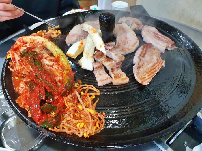 솥뚜껑 위에 올려진 삼겹살과 대파김치 및 배추김치 사진입니다.