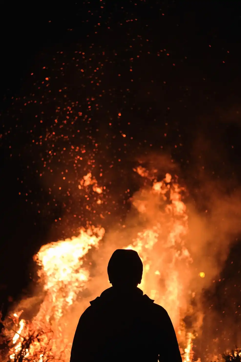 밤 중에 크게 타오르고 있는 불을 멍하니 바라보고 있는 한 남성이 있다.