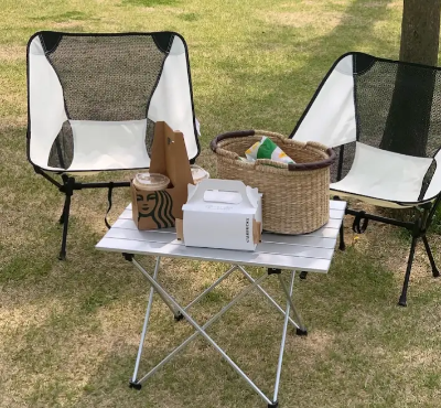 캠핑용 의자와 테이블&#44; 테이블위에 군것질거리와 음료가 있음