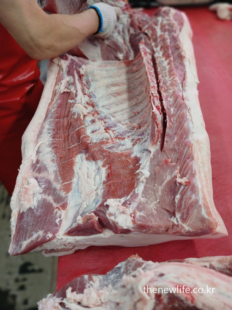 A butcher slicing a slab of pork belly on a red counter-정육점에서 돼지고기 부위를 발골하는 모습