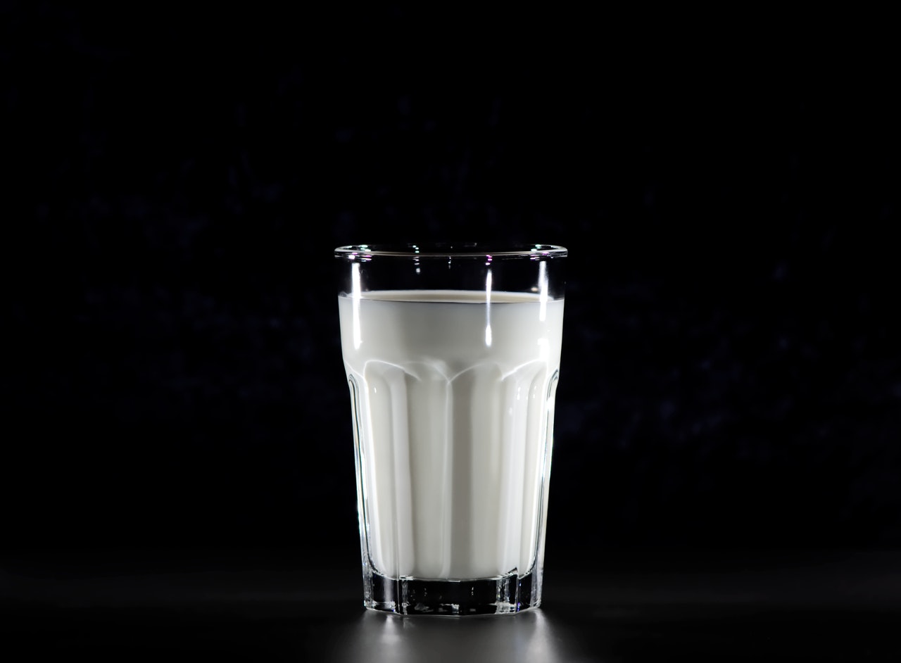 검은색 배경화면에 투명한 유리컵안에 하얀색 우유가 채워져 있는 사진