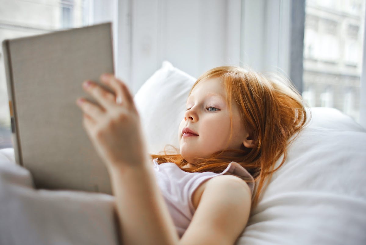 어린 여자아이가 누워서 책을 읽고 있다.