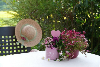 야외 테이블 위 분홍색 꽃화분과 빨간색 꽃화분 그리고 의자에 창이 넓은 모자가 걸려 있음