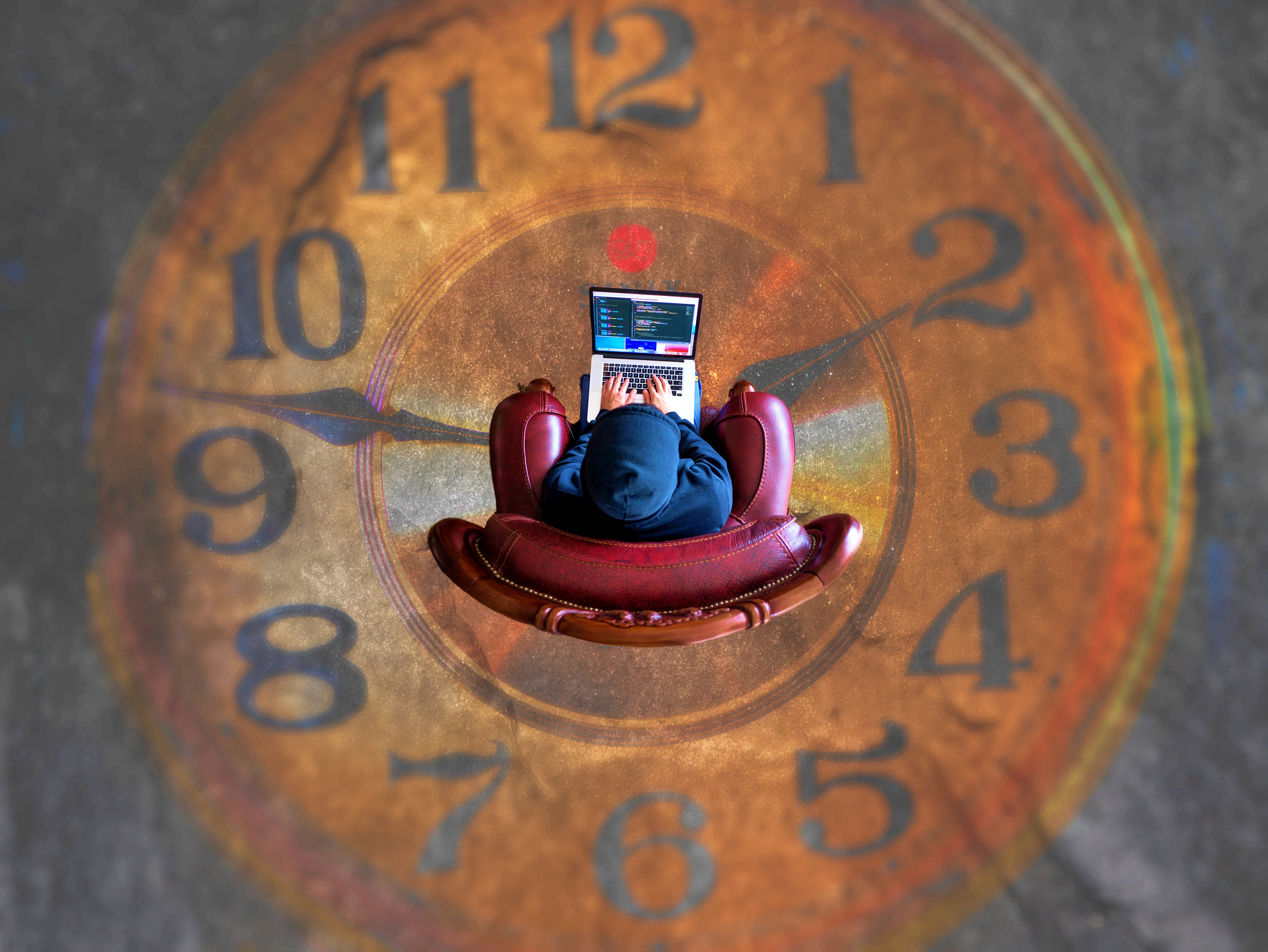 커다란 시계 위에서 의자에 앉아 노트북을 사용하는 사람