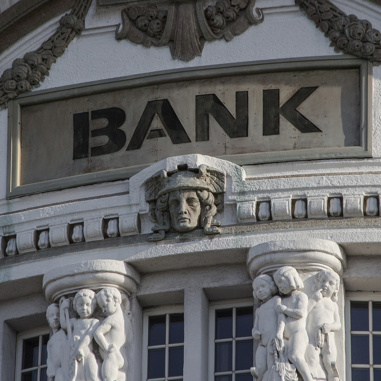콘크리트 건물에 bank라고 써있고 사람 형상의 조형물이 있는 그림