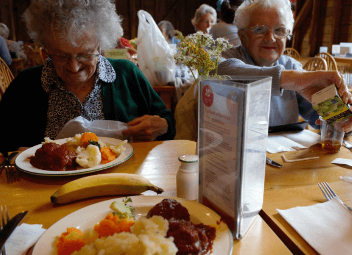 서양 흰머리의 할머니 두명이 식당에서 식사를 시작하려고 하는 중