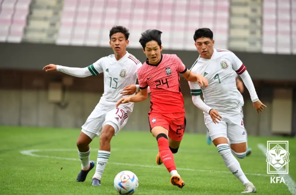 축구경기장 붉은 국가대표 유니폼을 입고 공을 드리블하는 양민혁과 흰유니폼을 입고 공을 양쪽에서 뺐으려는 상대선수 2명