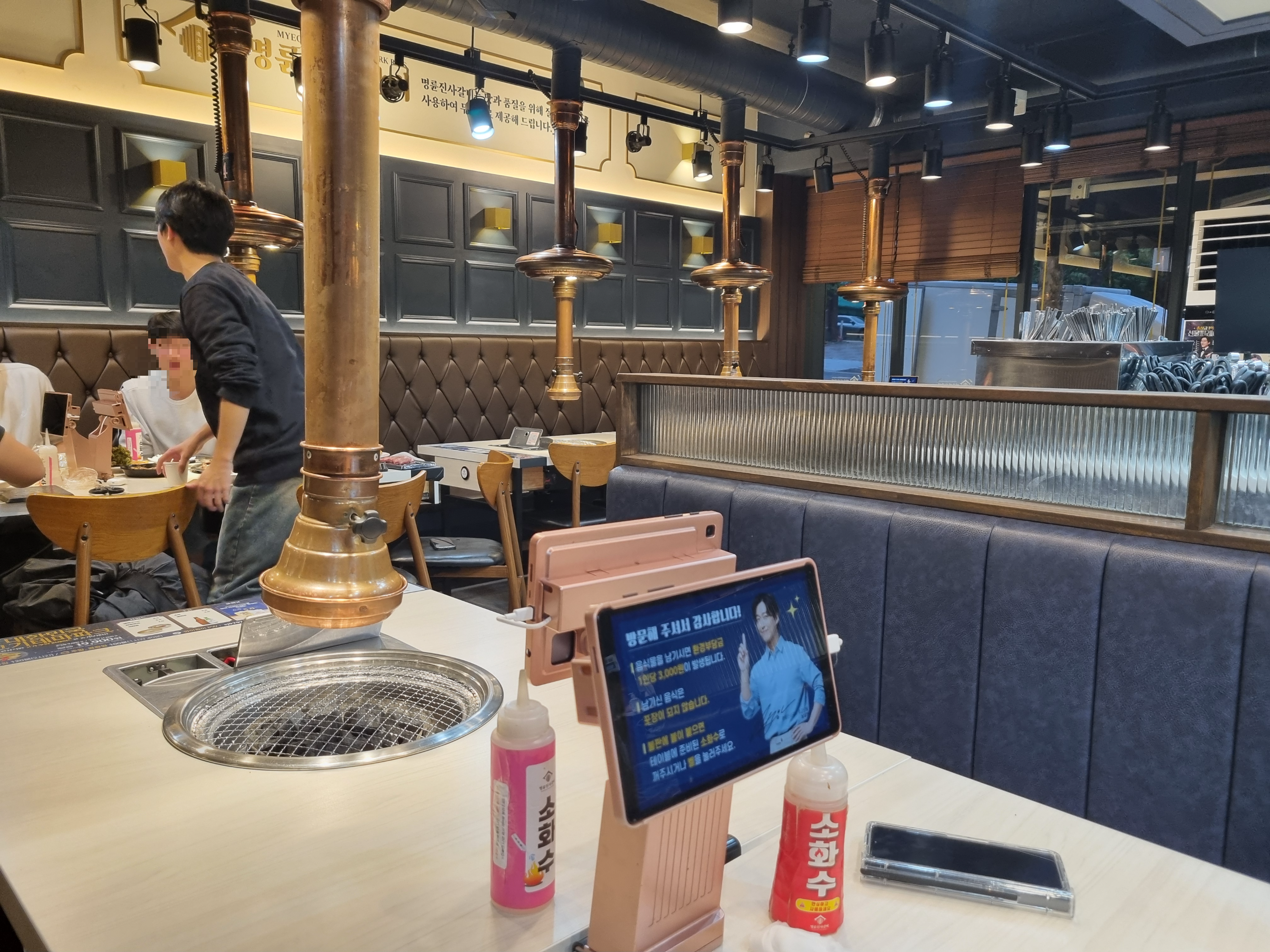 8인 테이블이 넓게 배치되어 있고, 테이블마다 후드가 달려 있는 매장 내부