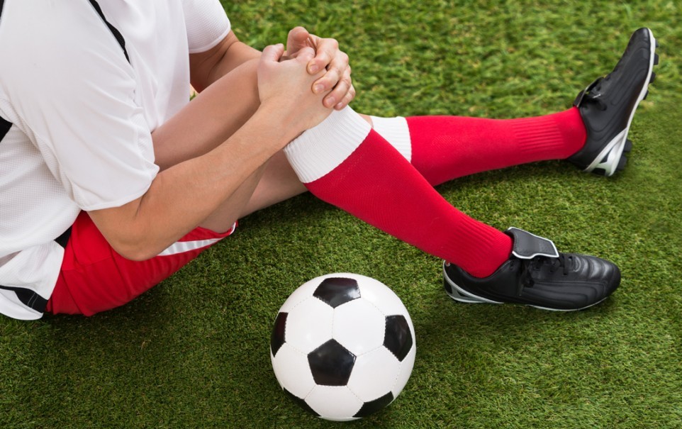남성이 축구를 하다가 무릎 부상으로 무릎을 잡고 앉아 있다