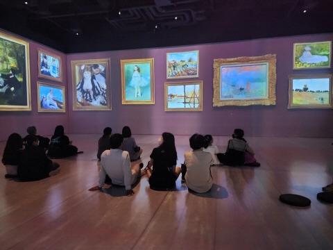 모네 인사이드 전시의 한 장면. 스크린에 모네의 대표작들이 떠 있고 사람들은 바닥에 앉아 관람하고 있다.