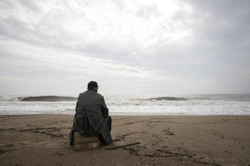 바닷가 모래 위에 홀로 앉아 있는 남성 노인