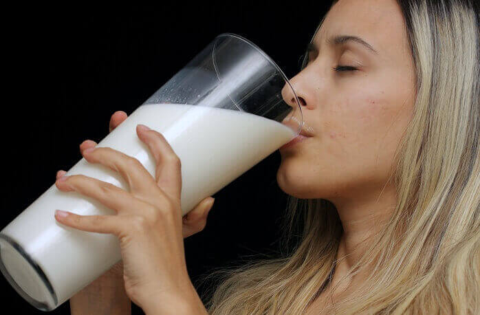 금발머리 여자가 세로로 긴 큰 유리잔에 가득 담긴 우유를 마시고 있는 모습