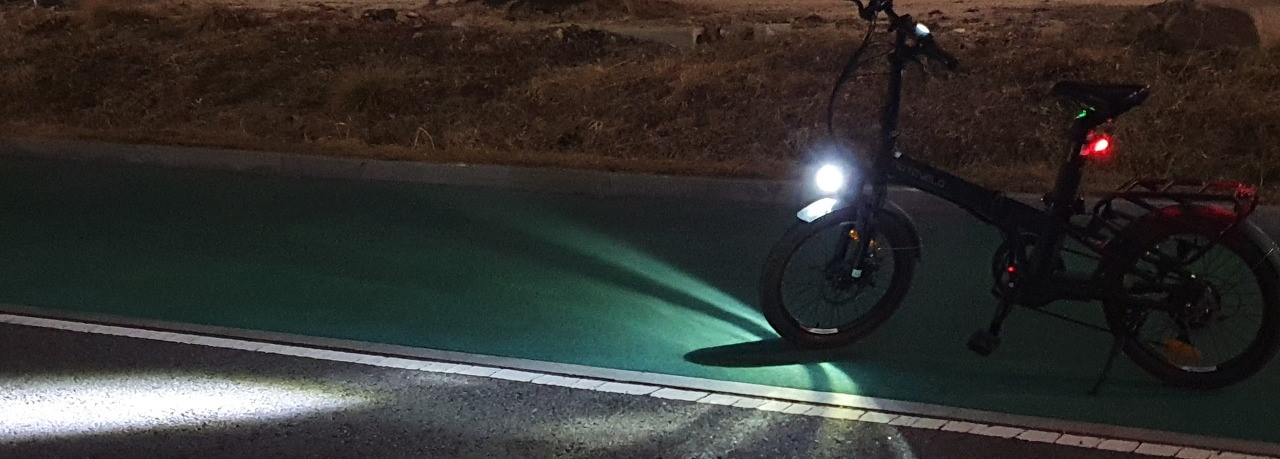 어두운 밤길&#44; 자전거길에 세워놓은 전기자전거&#44; 환하게 비추는 헤드라이트&#44; 빨간 백라이트&#44; 좌우로 곧게 뻗은 자전거길 표시 백색라인&#44;