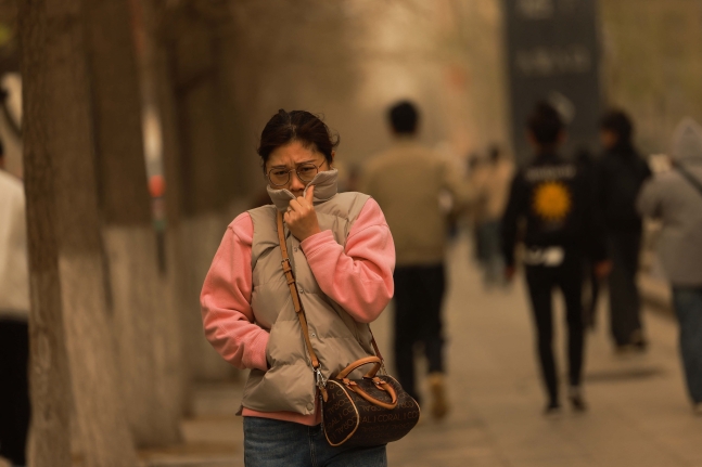 11일 중국 랴오닝성 선양 시내에서 한 여성이 옷깃으로 입을 막고 걷고 있다