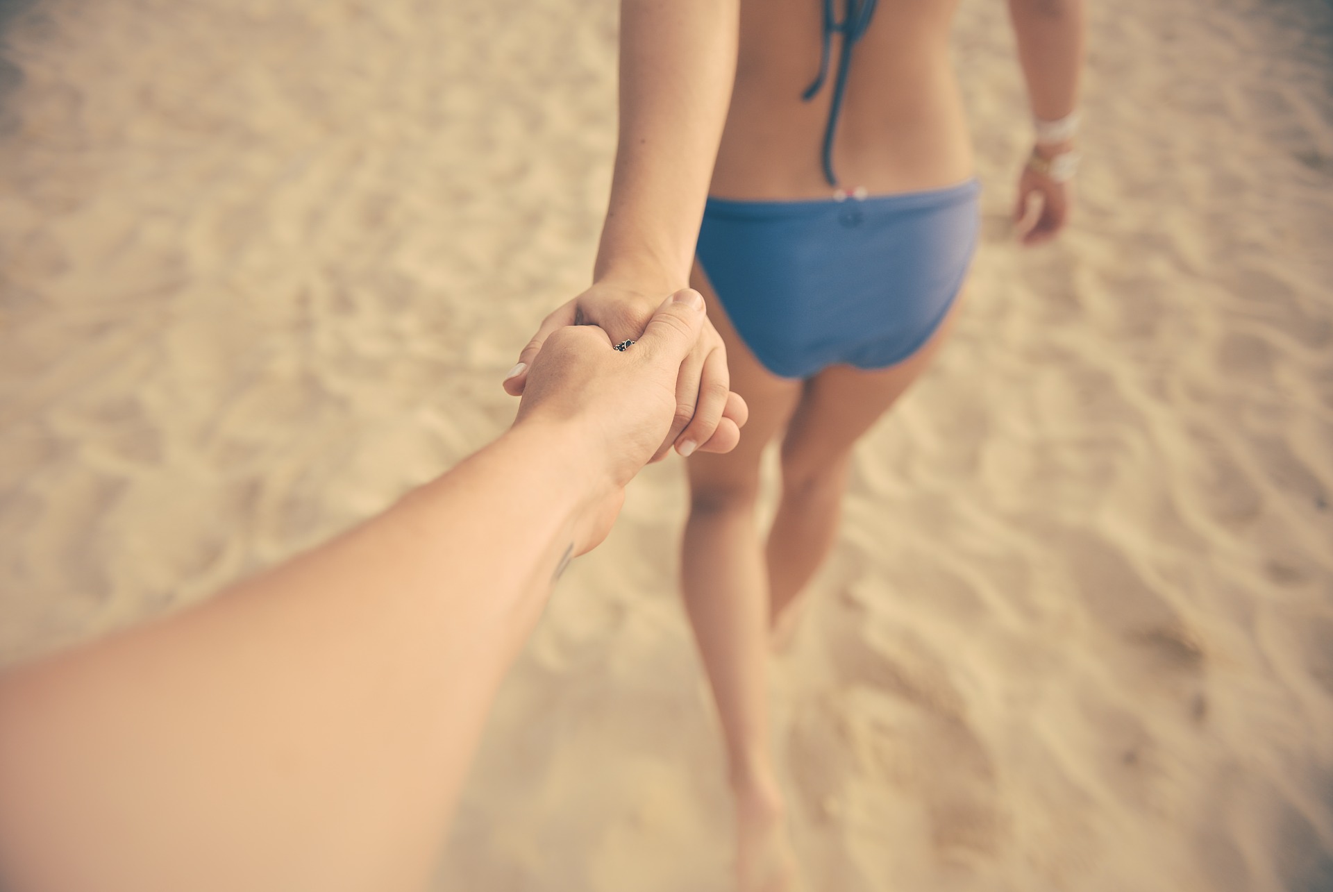 해변에서 여자가 앞서가고 뒤에서 남자가 손잡고 따라가는 사진