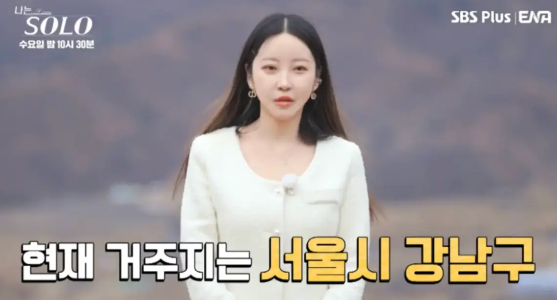 야산배경 흰정장을 입은 여자가 말하는 모습 아래 흰글씨 현재 거주지는 서울시 강남구
