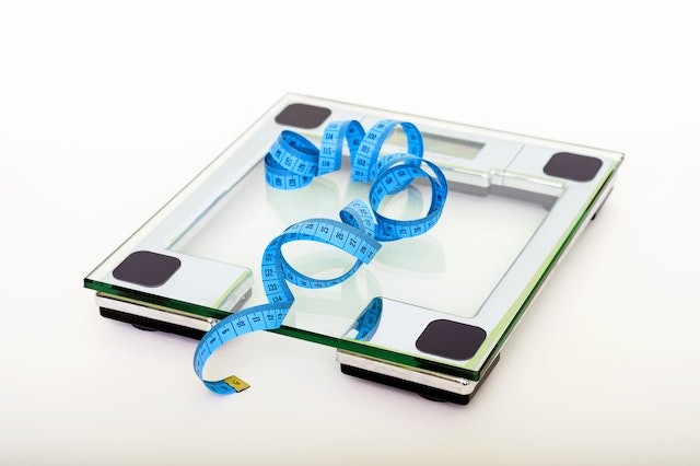 상판이 유리로 된 체중계와 그 위에 놓인 파란색 줄자의 사진