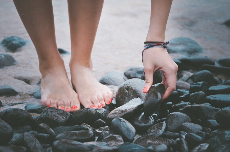 바닷가에서 검은 색깔 돌을 만지고 있는 사람 손 사진
