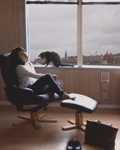 고양이가-창문에서-놀고있는-방에서-한여자가-의자에서-휴식을-취하는-모습-덴마크휘게