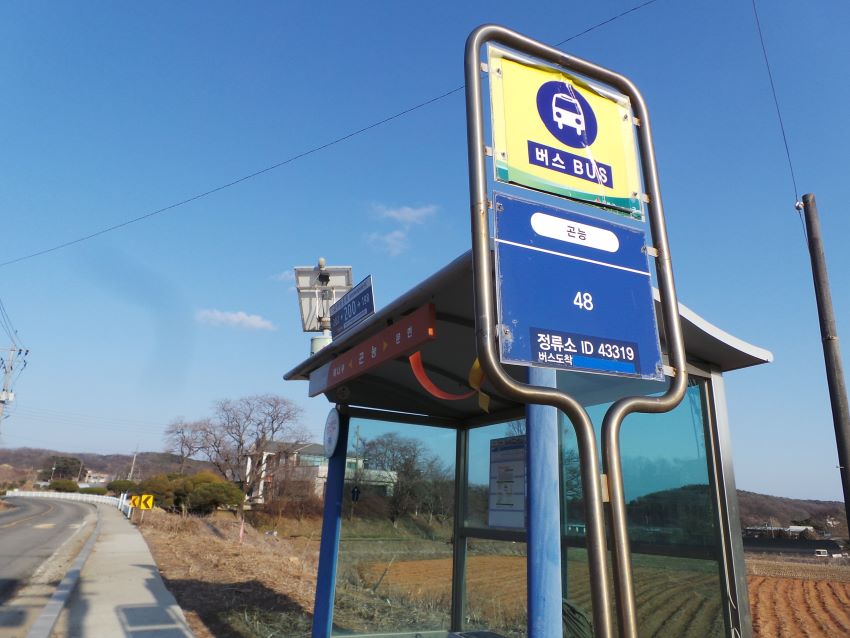 푸른 하늘을 배경으로 한 버스정류장 안내판과 부스&#44; 푸른 바탕에 흰글씨&#44; 올려다 본 사진&#44; 왼쪽에는 차로&#44;