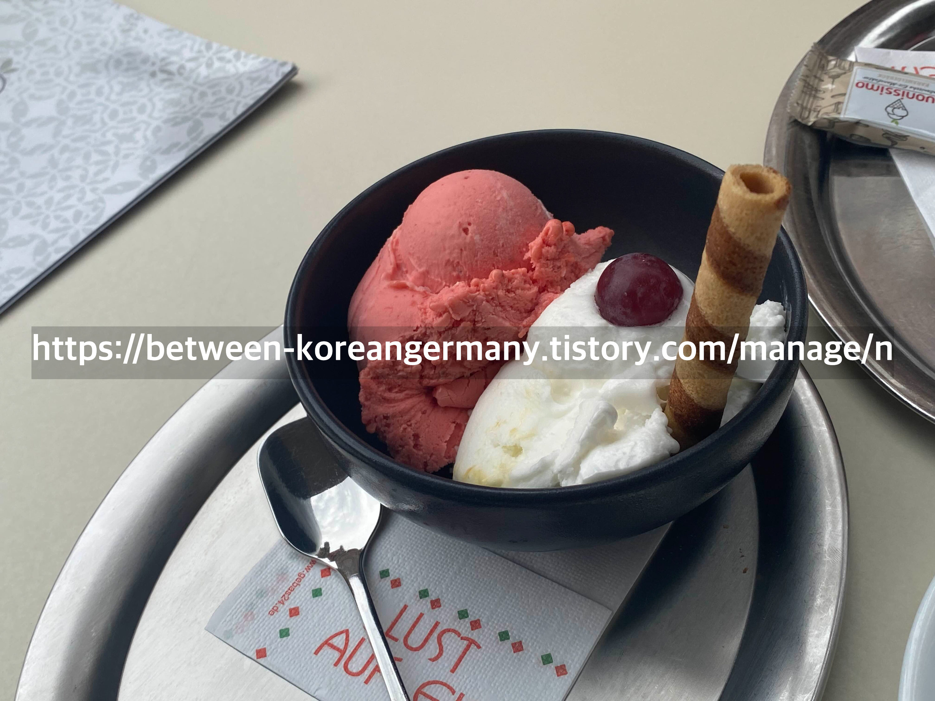 검은 색 그릇 안에 담긴 하얀색&#44; 핑크색 아이스크림과 흰색 아이스크림 위에 꽂힌 원통형의 와플 과자