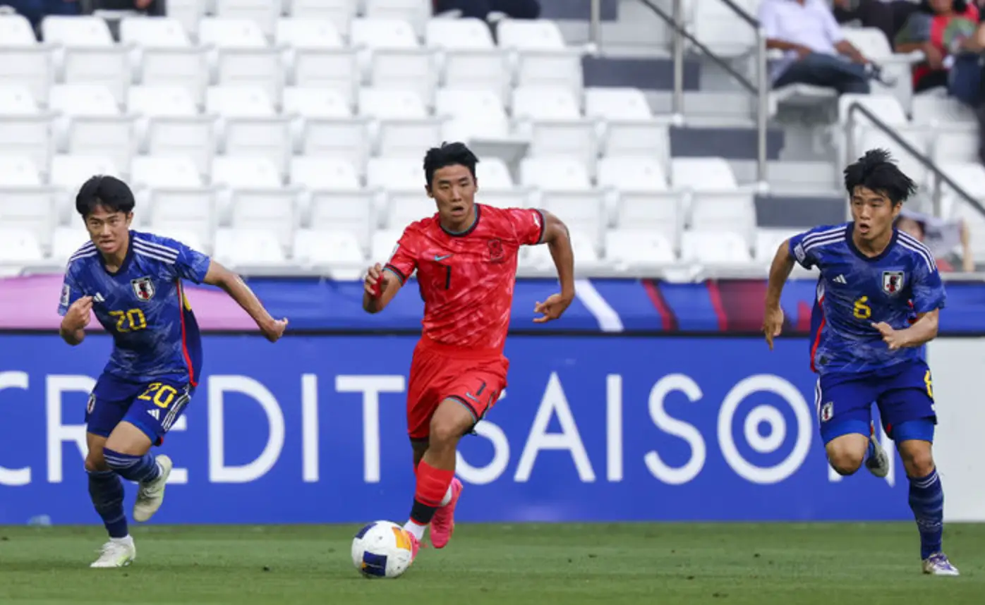 파리-붉은 유니폼을 입은 국가대표 선수가 공을 차며 달려나가는 모습과 그의 양옆으로 파란 유니폼을 입은 일본선수들이 따라붙는 모습