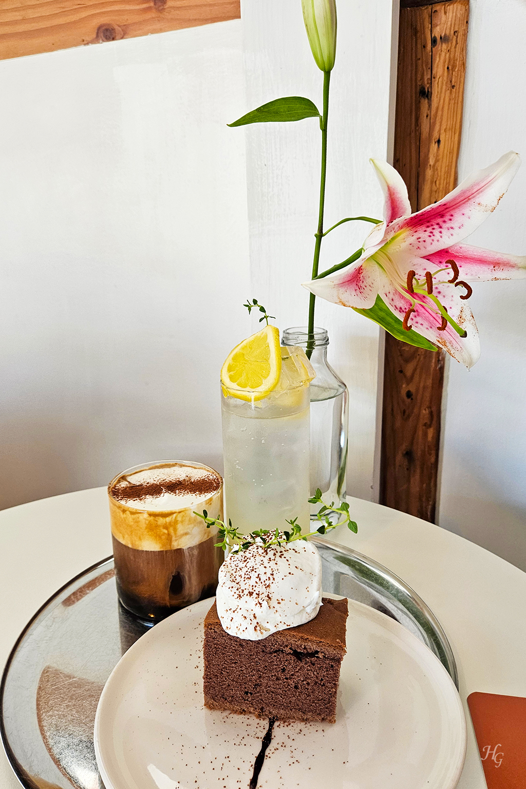 흰 테이블 위에 올라가 있는 꽃과 크림 커피와 진저레몬 음료와 진저브레드