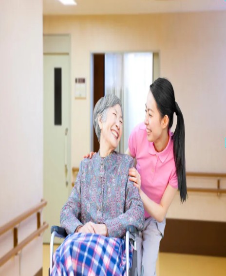 휠체어에 앉아 미소 짓는 환우님과 다정한 눈빛을 나누는 요양보호사의 모습