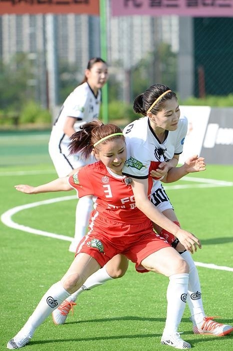 붉은 유니폼과 흰 유니폼을 입은 서로 다른 팀의 두 여성이 축구 경기에서 서로 몸싸움을 하고 있다.