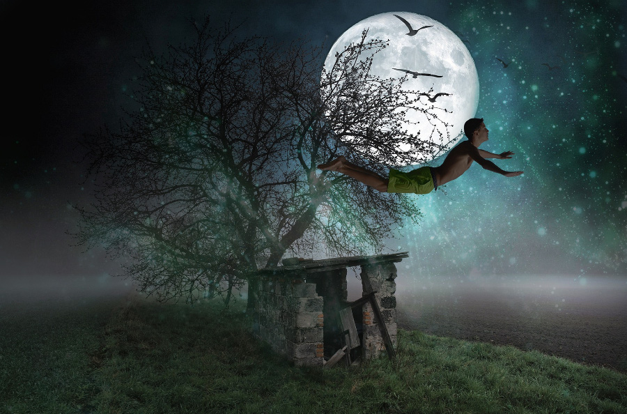 젊은 남성이 깊은 밤에 달을 배경으로 반바지만을 입고 새와 함께 하늘을 날고 있는 것을 찍은 사진