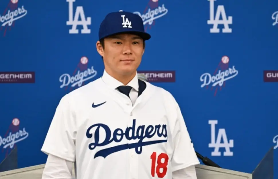 파란색 원단 위 흰글씨 LA dodgers 앞 흰유니폼 파란 야구모자를쓰고 미소지으며 서있는 야마모토