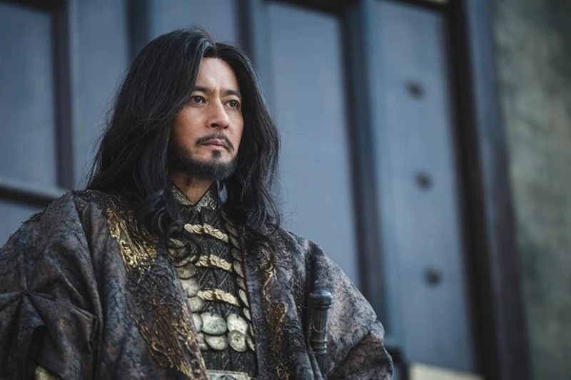 거대한 철문을 배경으로 화려한 왕의 복장과 긴 머리를 내려 트리고 위엄있게 앉아 있는 아라문의 검의 타곤 캐릭터